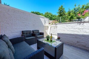 A patio with wicker furniture, a glass table, and a bottle of wine.