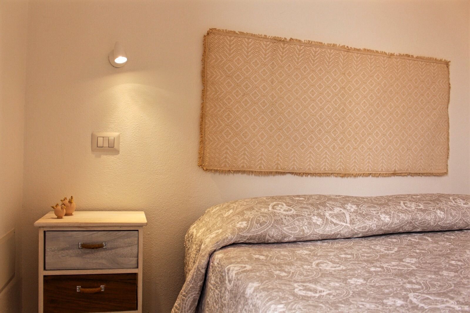 Ein Schlafzimmer mit einem Bett, einem Nachttisch mit Schubladen, einer Wandleuchte und einer Wanddekoration.