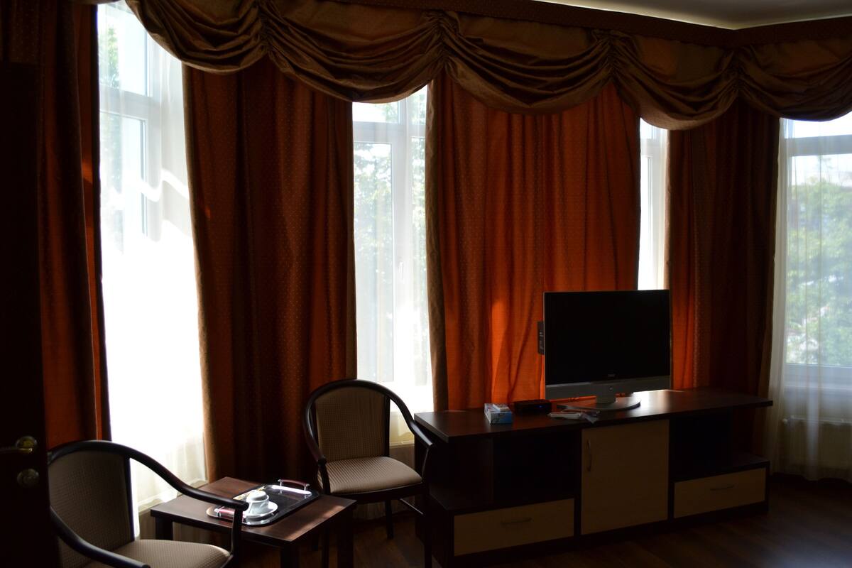 A hotel room with a TV on a wooden cabinet, a chair, and a table with a tray.