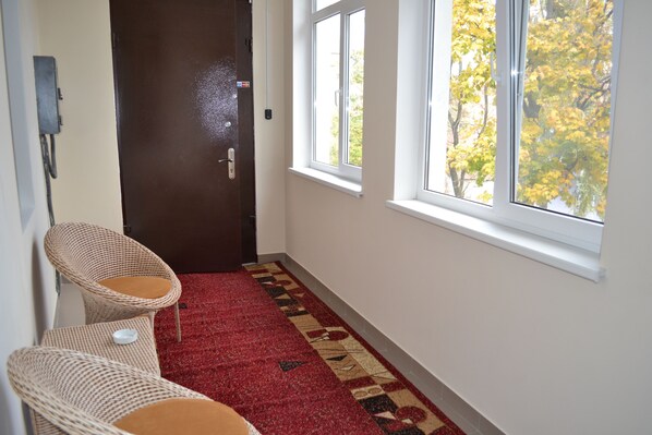 A hallway with a red carpet, wicker chairs, a door, and windows with a view of trees. - Paloma House (Kharkiv)