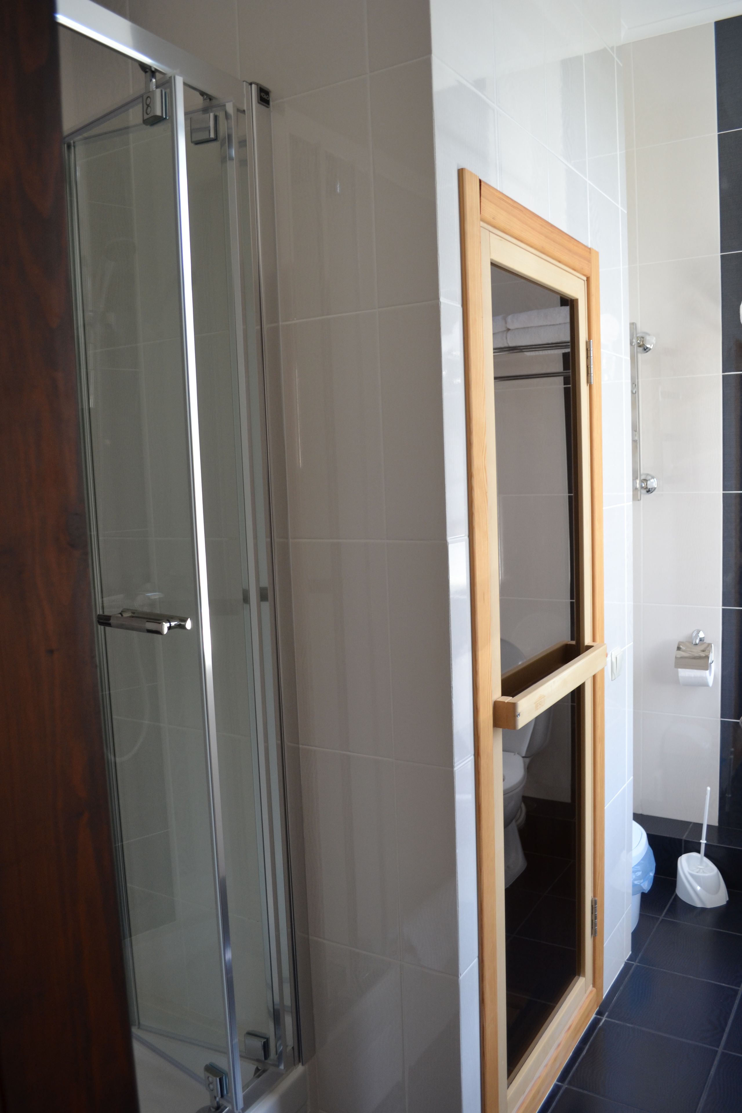 A bathroom with a glass-enclosed shower, a wooden-framed mirror, and a toilet.