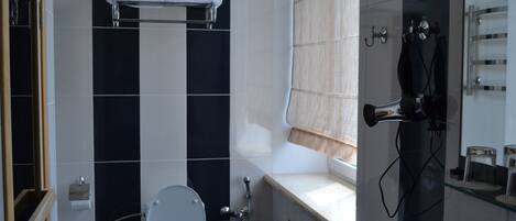 Une salle de bain comprenant des toilettes, un porte-serviettes, un espace douche et une étagère en verre où sont rangés les articles de toilette.
