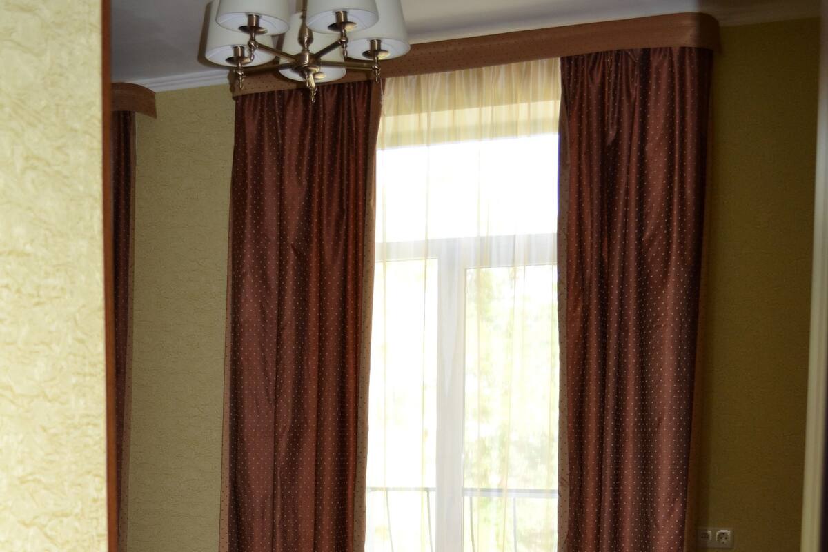 A room with wooden flooring, a chandelier, and a window with curtains.