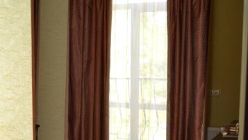 A room with wooden flooring, a chandelier, and a window with curtains.