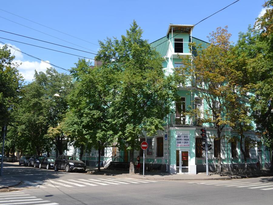 A multi-story building with a green roof and white walls, located at a street intersection with a no entry sign.