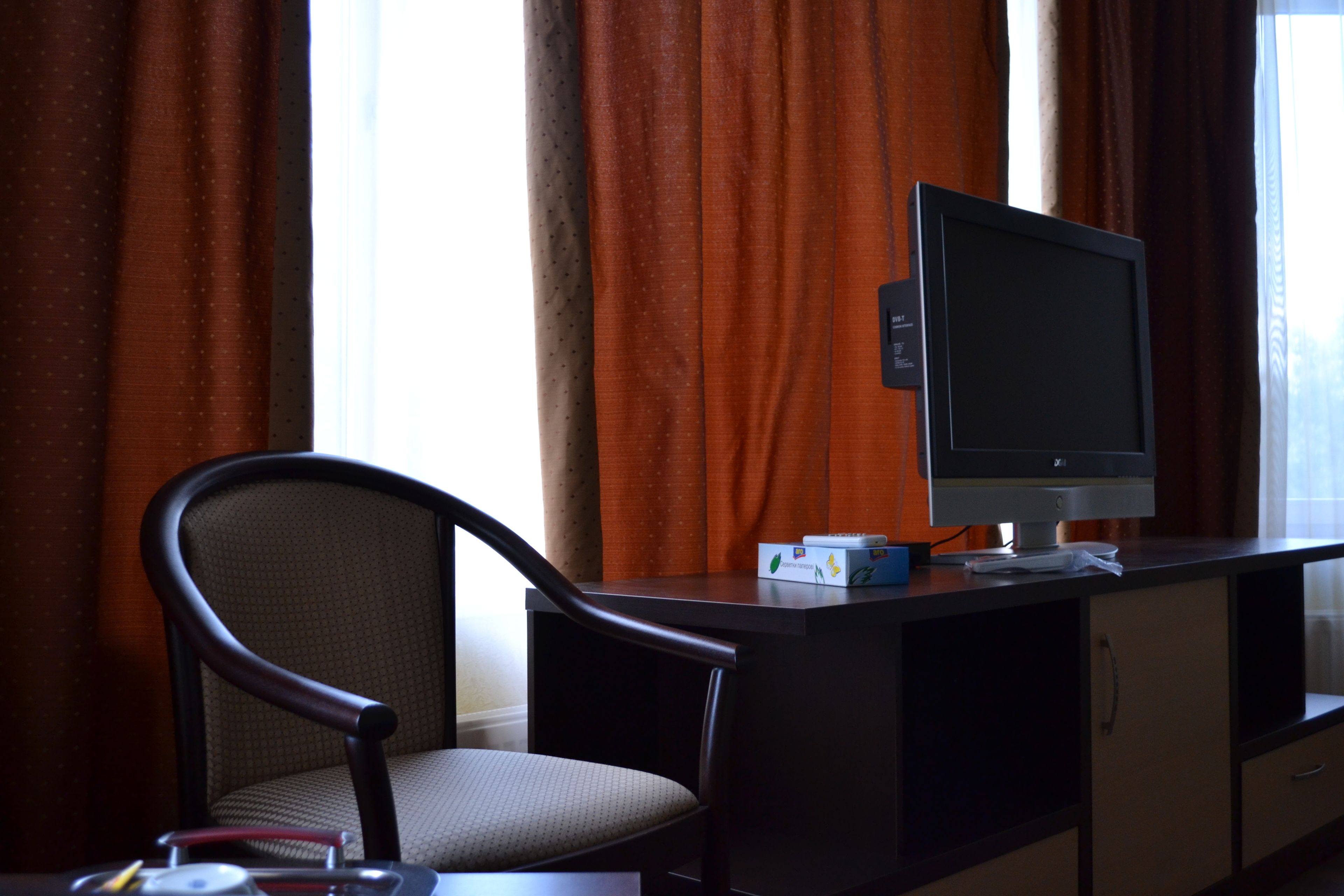 A hotel room with a desk, a television, a chair, and a window with curtains.