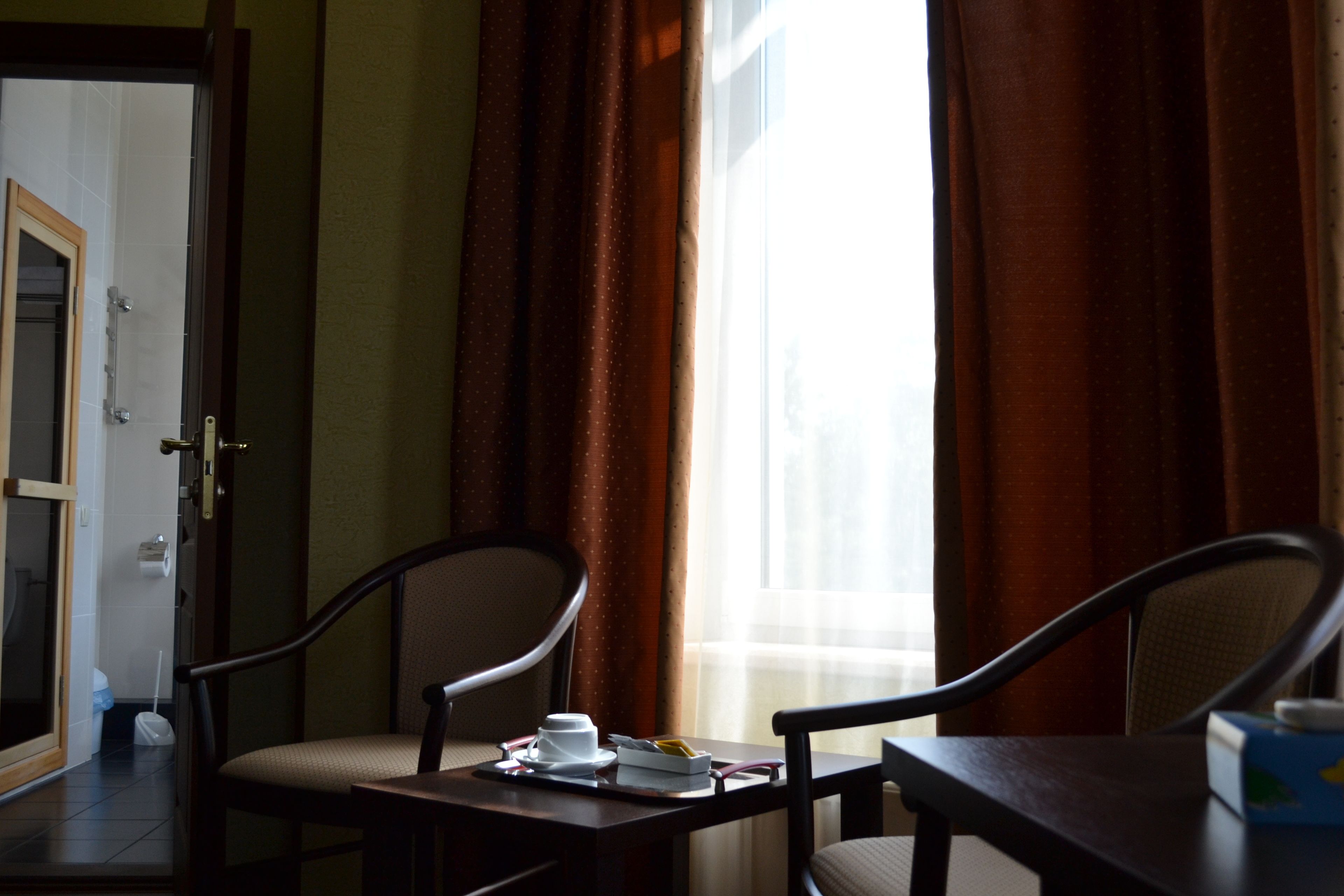 A hotel room with a view of the outdoors, a dining table with a cup and saucer, and two chairs.