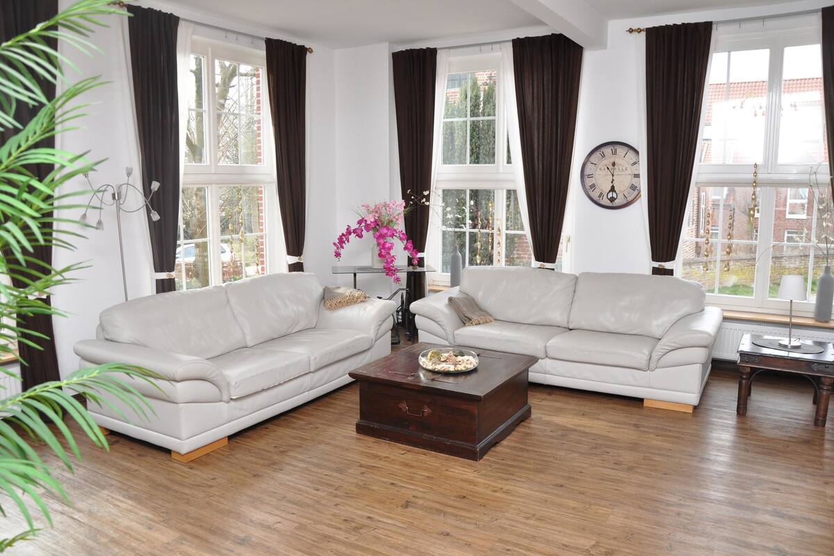 A living room with two white sofas, a wooden coffee table, and a large window with curtains.