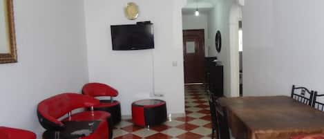 A dining area with a checkered floor, red and black chairs, a wooden table, and a flat-screen TV mounted on the wall.