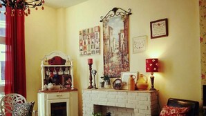Un salón acogedor con chimenea, un armario blanco con adornos, una cortina roja y un sillón negro.