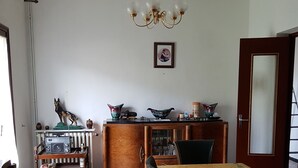 Un coin repas avec une table, des chaises, une radio posée sur une étagère et un lustre.