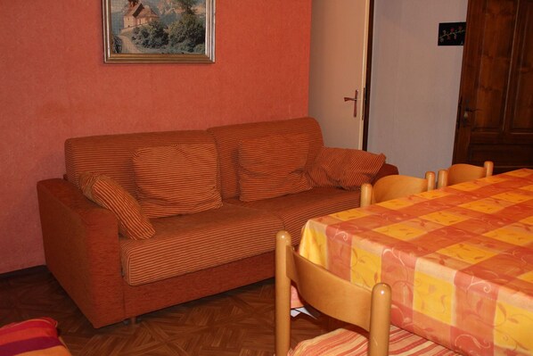 Une pièce avec un canapé à rayures, une table en bois recouverte d’une nappe à carreaux, une porte en bois et un tableau encadré accroché au mur.