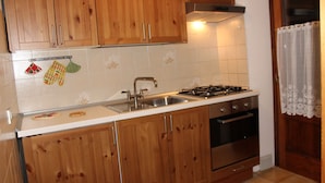 Une cuisine avec des meubles en bois, un évier en acier inoxydable, une cuisinière à gaz et un dosseret carrelé.
