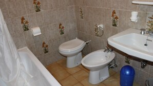 Une salle de bain avec une baignoire, deux toilettes, un bidet et un lavabo.