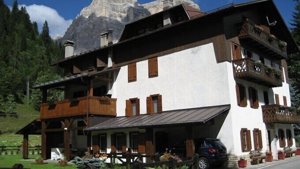Un chalet traditionnel doté d’un balcon en bois, de murs blancs et surplombant un paysage montagneux.