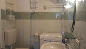 A small bathroom with a toilet, sink, and mirror. There are shelves above the toilet and a towel rack. - Casa Rosina 6 (Val di Zoldo)