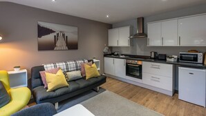 A modern living room with a sofa, a dining area with a kitchen, and a painting on the wall. - The Hive Apartment (Stockport)