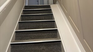 A staircase with carpeted steps and white handrails, leading to a door at the top. - The Hive Apartment (Stockport)