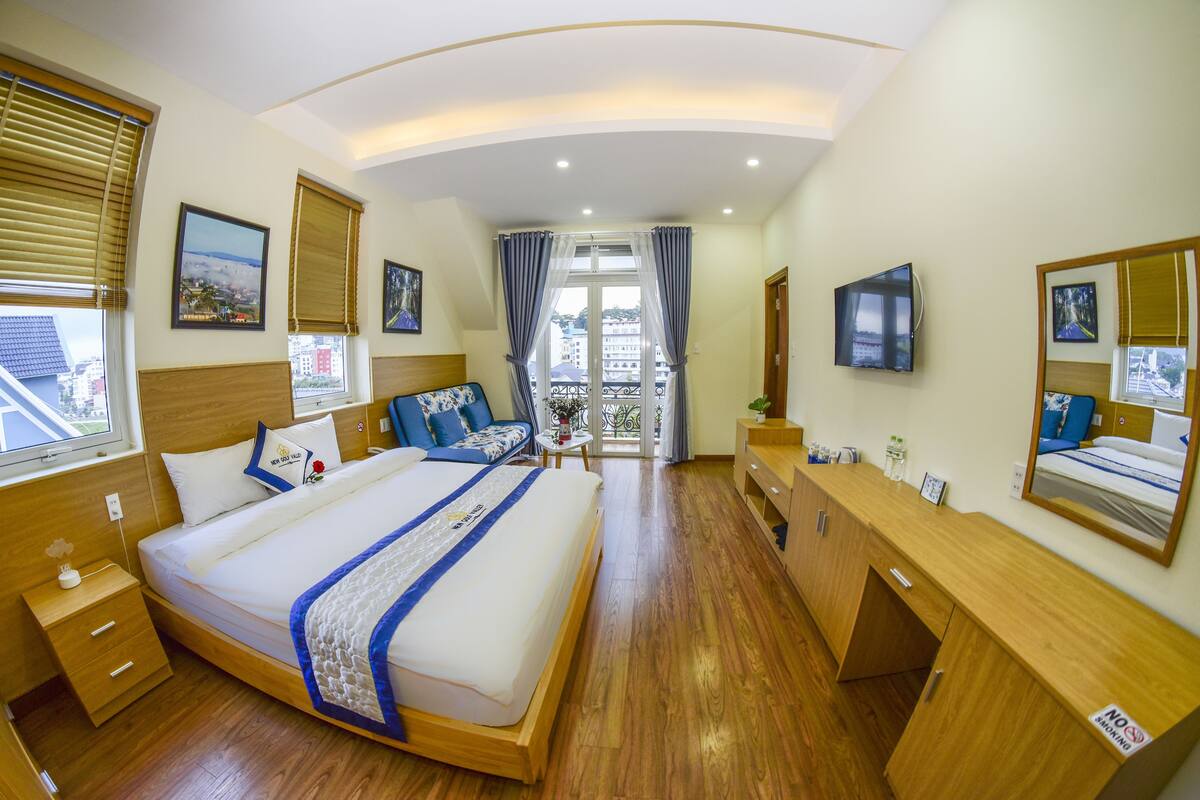 Quarto de hotel com uma cama grande, móveis de madeira, televisão e varanda com vista.