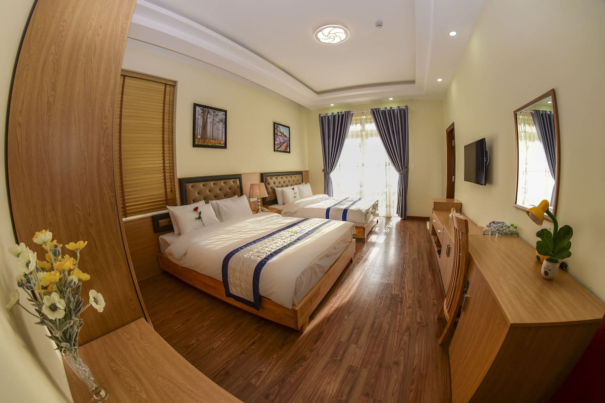 Quarto de hotel com duas camas, piso de madeira, uma mesa, um espelho e um vaso com flores.
