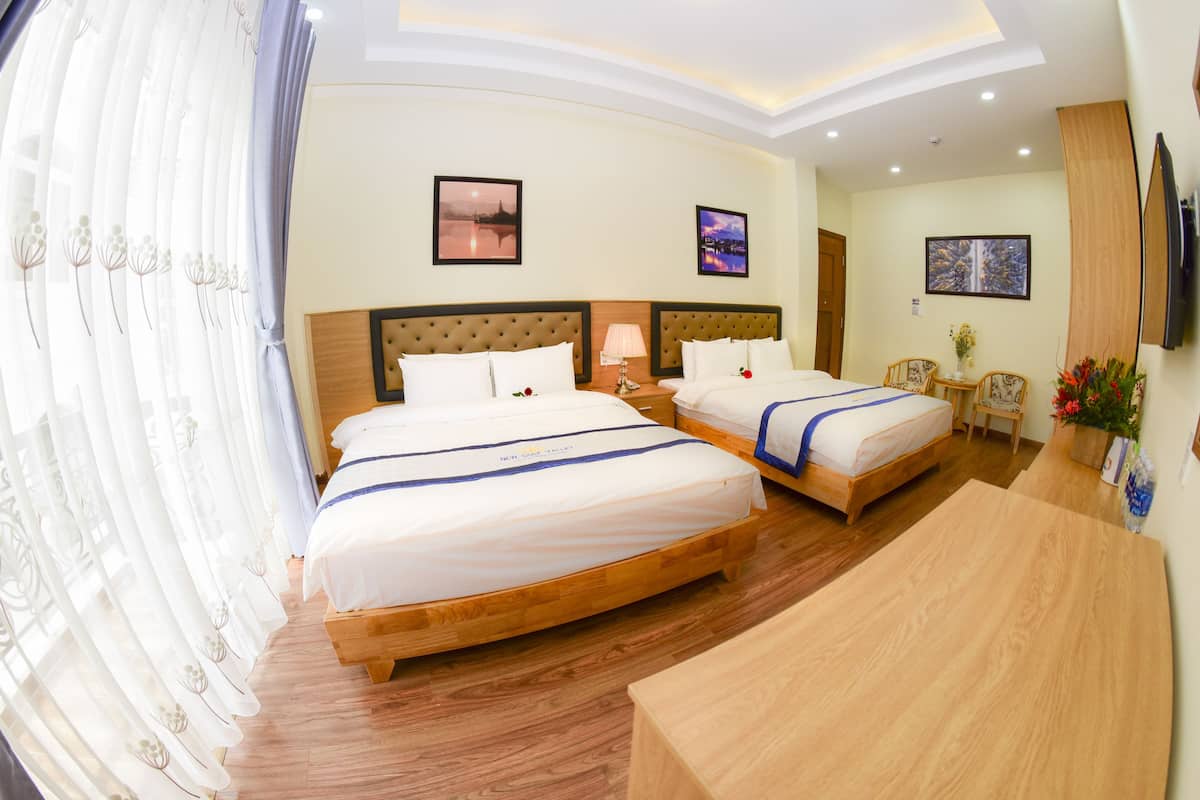 Quarto de hotel com duas camas, piso de madeira, televisão e obras de arte nas paredes.