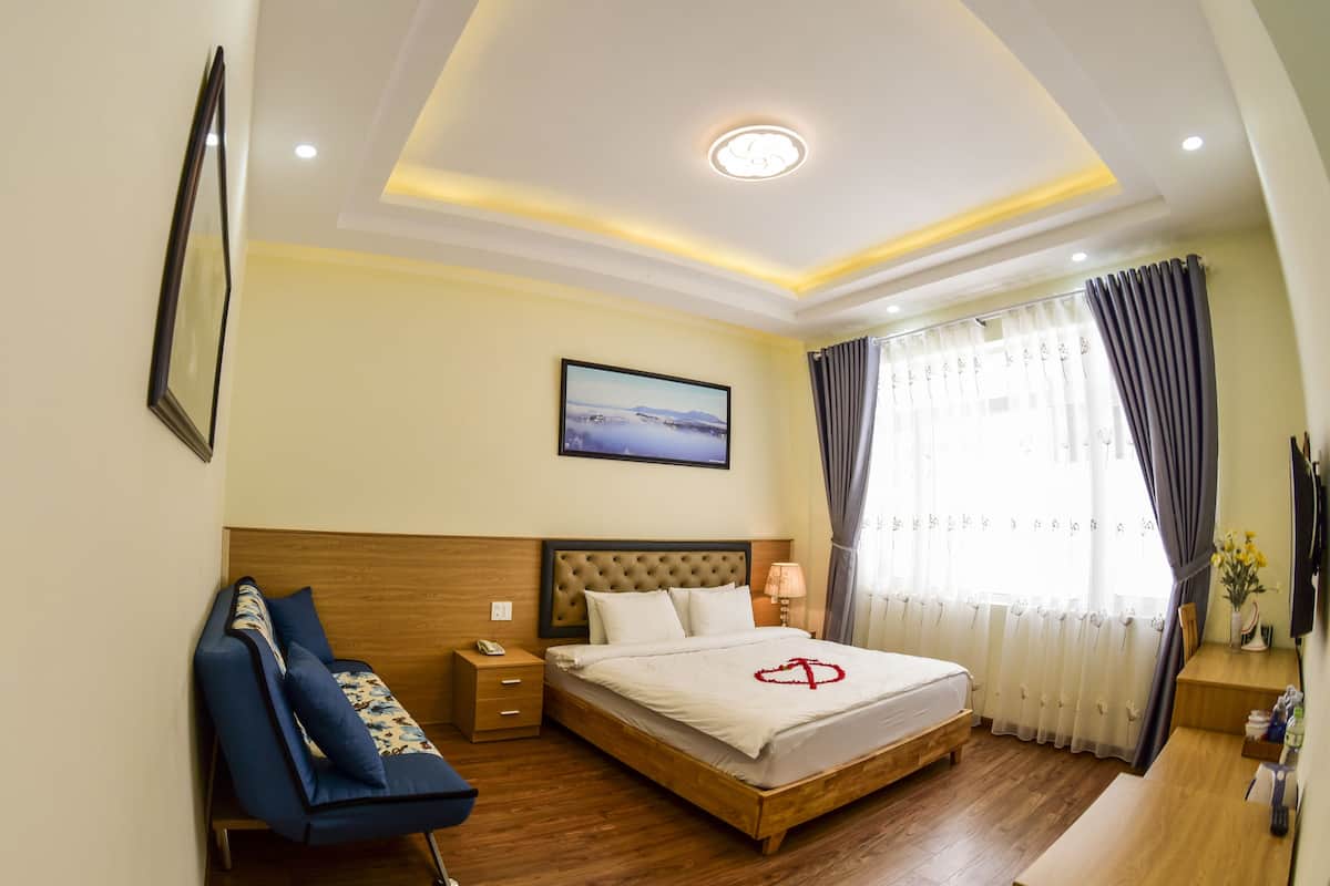 Quarto de hotel com cama, mesa de cabeceira, abajur e vista para o exterior pela janela.