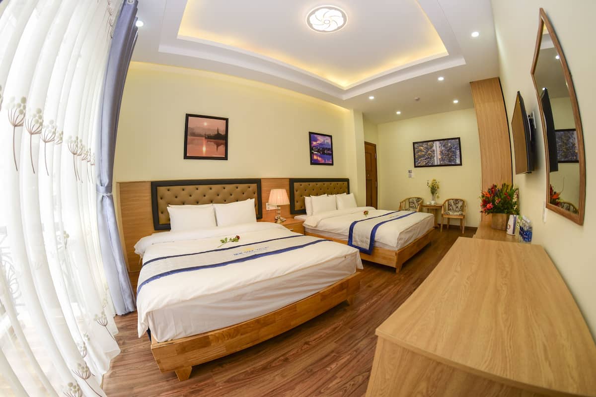 Quarto de hotel com duas camas, cabeceiras de madeira, uma escrivaninha de madeira e um espelho grande.