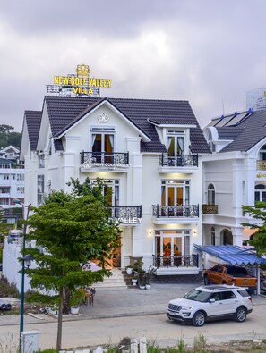 A multi-story building with balconies, a sign reading "New Golf Valley Villa," and a white SUV parked in front. - New Golf Valley Hotel (Xuan Huong - Da Lat)