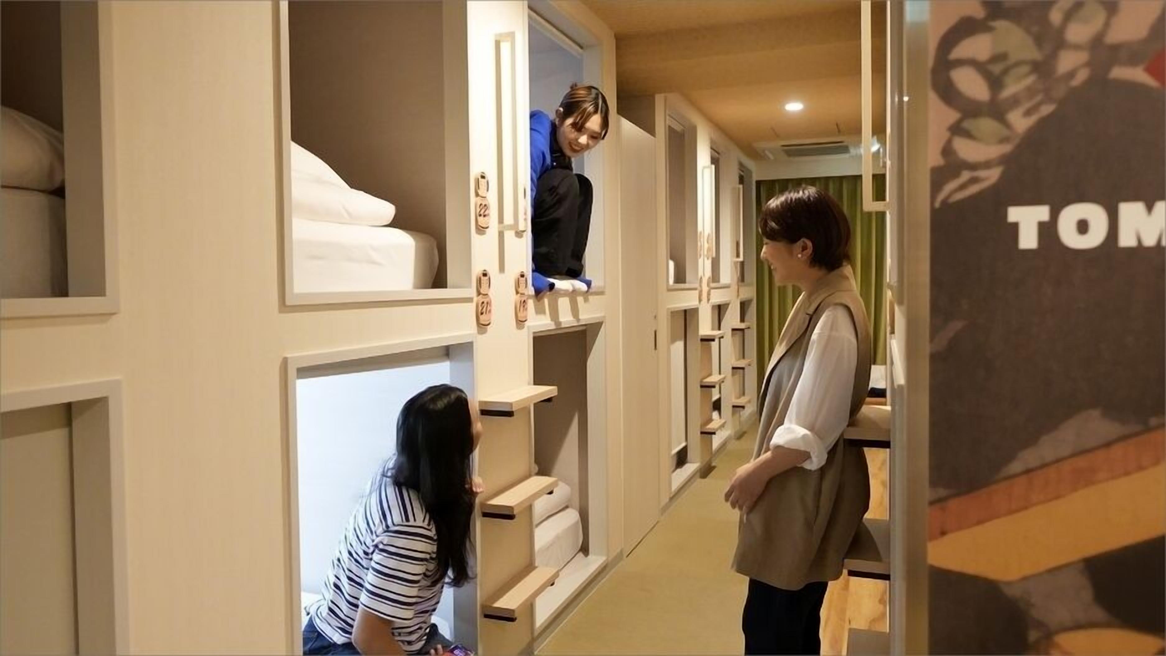 A hotel corridor with individual rooms, each with a bed and a shelf with shoes.