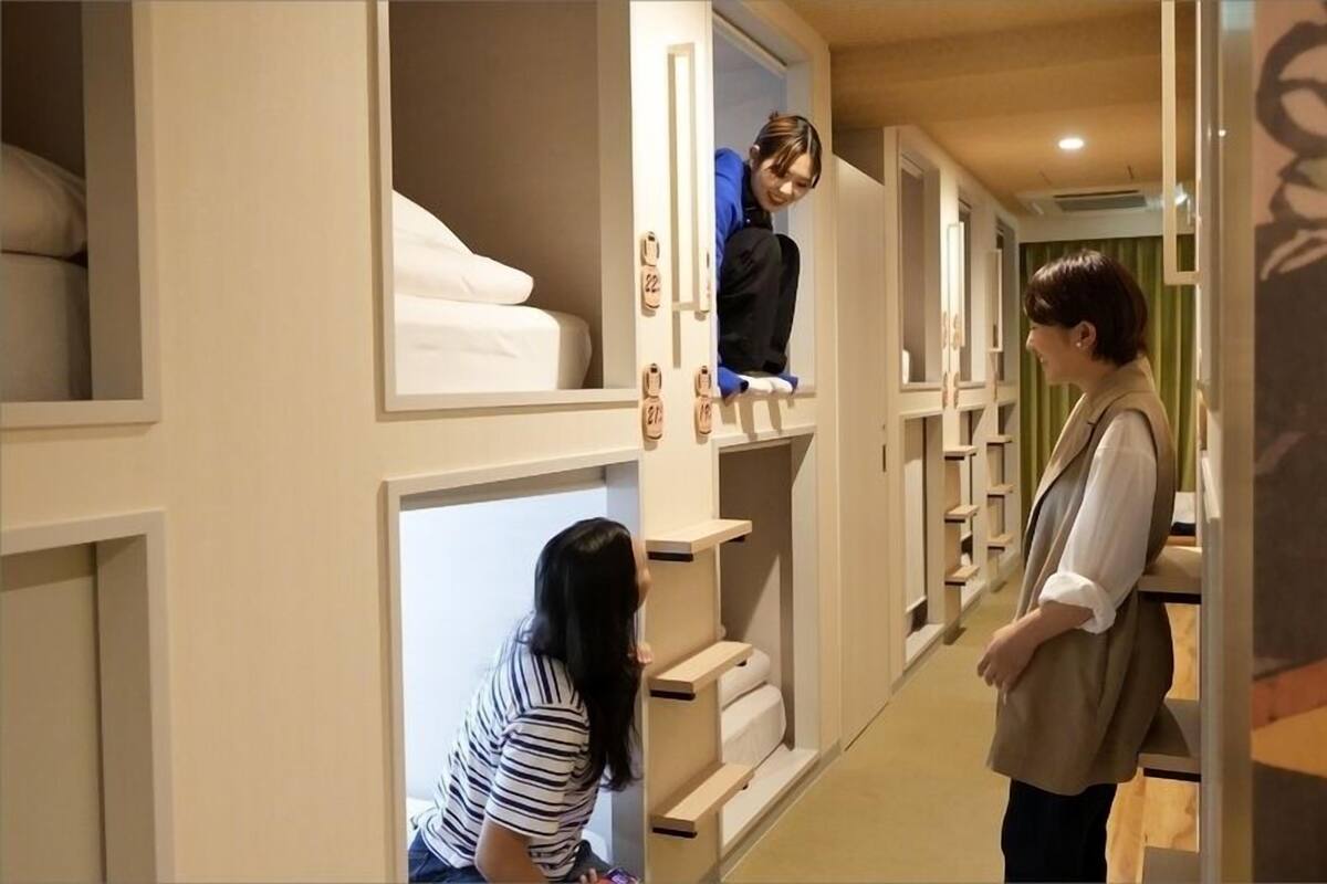 Un pasillo de hotel con habitaciones individuales, cada una con una cama y un estante para zapatos.