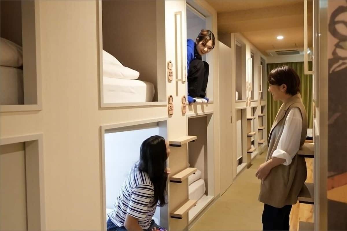 Corredor de hotel com quartos individuais, cada um com uma cama e um armário com sapatos.