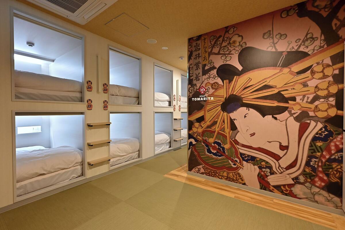 Una habitación de hotel con literas, un mural y un letrero que dice 'Stay Tomariya'.