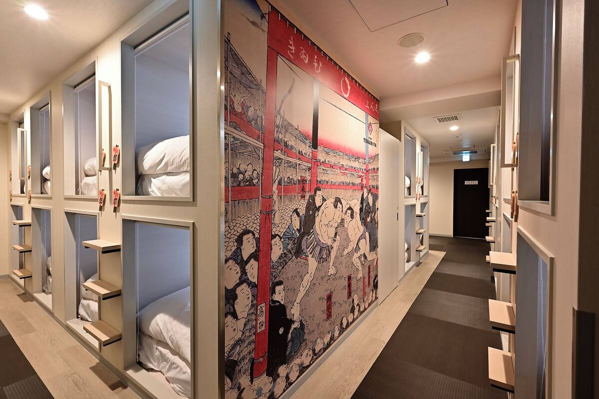 Pasillo de hotel con literas, un gran mural de luchadores de sumo y un diseño moderno.