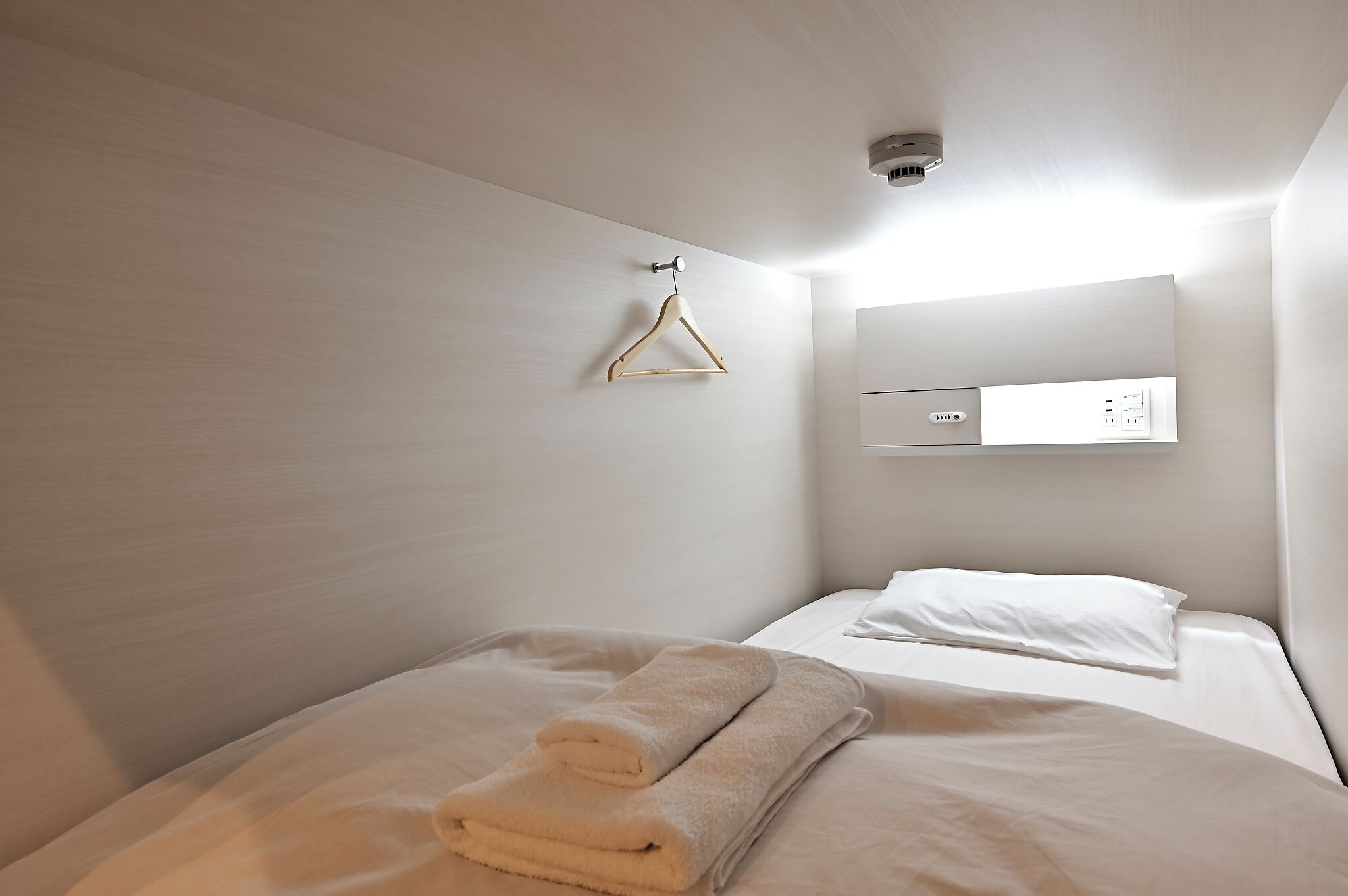 A hotel room with two beds, a wall-mounted power outlet, and a hanging light fixture.
