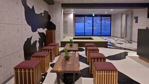 A modern interior with wooden tables and red cushioned seating, a large wall mural, and a view through glass doors. - Hotel Tomariya Ueno - Hostel (Tokyo)