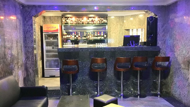 A bar area with a marble counter, bar stools, and a seating area with a sofa and ottomans. - Elicris Hotel (Lagos)
