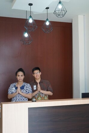 A reception desk with a wooden panel wall and three geometric pendant lights. - Gold Line Guest House (Pontianak)