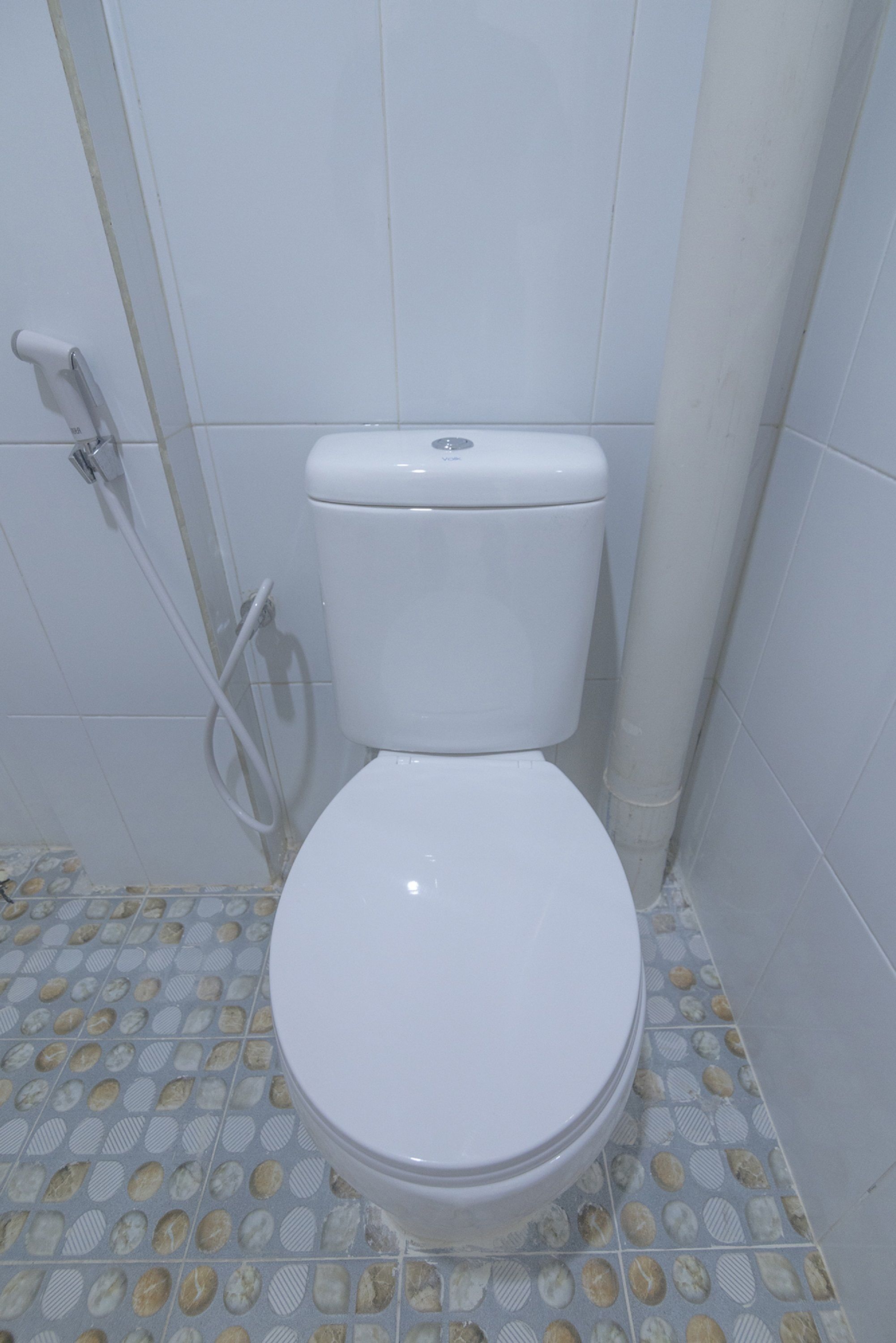 Sanita branca com cisterna e assento, um cano branco e um chão em azulejo com padrão de formas ovais.