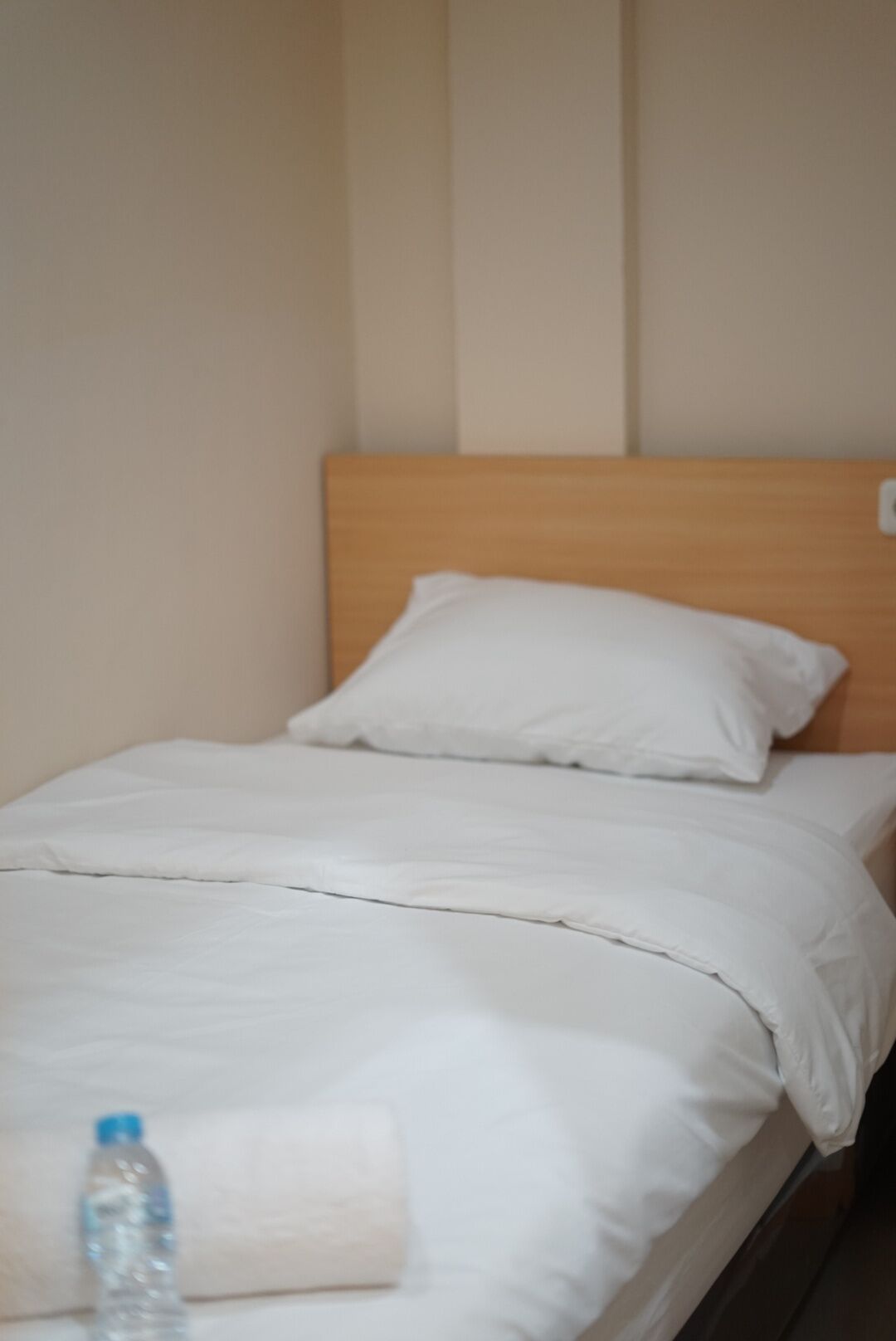 Una cama con ropa de cama y almohadas blancas, un cabecero de madera y una botella de agua en el suelo.
