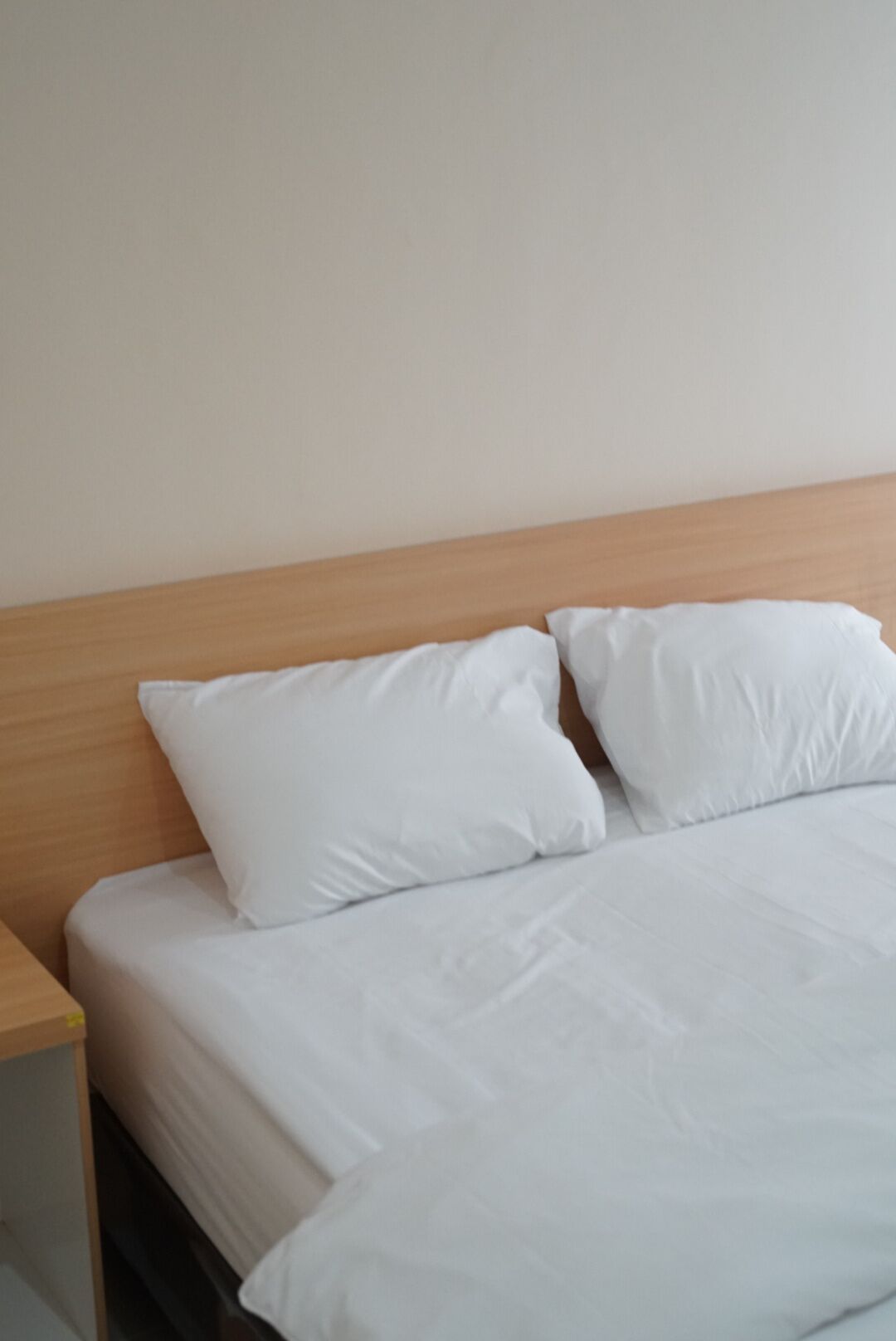 Ein Bett mit weißer Bettwäsche und Kissen, ein Holz-Kopfteil und ein Nachttisch links.