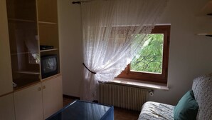 A room with a wooden cabinet, a television, a window with lace curtains, a radiator, and a bed with a floral bedspread. - Casa Rosina 8 (Val di Zoldo)