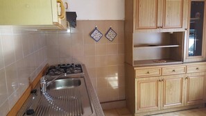 A kitchen with a gas stove, stainless steel sink, wooden cabinets, and two decorative wall hangings.