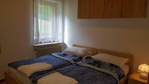 A bedroom with two beds, a window with lace curtains, a radiator, and a bedside lamp. - Casa Rosina 8 (Val di Zoldo)