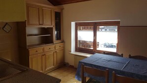 A kitchen with wooden cabinets, a window with a view of the outside, and a table with chairs. - Casa Rosina 8 (Val di Zoldo)