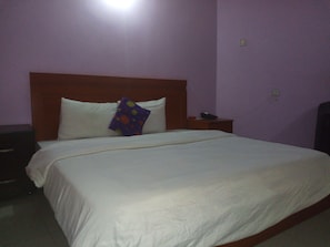 A neatly made bed with white bedding and a purple pillow with a polka dot pattern. - Flamingo Hotel & Suites (Lagos)