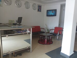 A reception area with a reception desk, multiple clocks, a television, and red and black chairs. - Flamingo Hotel & Suites (Lagos)