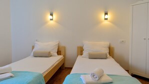 A room with two single beds, each with a wooden headboard, white bedding, and a blue throw blanket. There are wall-mounted light fixtures above each bed. - Golden B&B (Split)