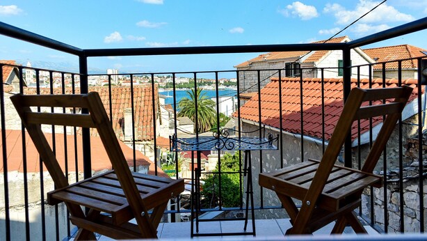 A balcony with two wooden chairs and a metal table, overlooking a coastal town with red-roofed buildings and a blue sea. - Golden B&B (Split)