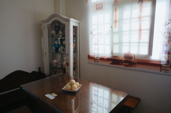 Una habitación con una mesa de madera, un aparador blanco con puertas de cristal y una ventana decorada.