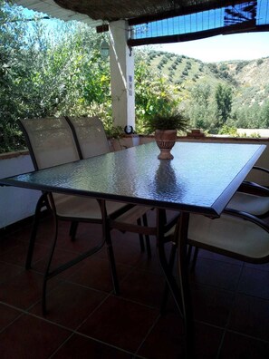 An outdoor patio with a table and chairs, a potted plant, and a view of a hilly landscape. - Casa Rosa (Almedinilla)